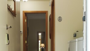 Un pasillo con una lámpara en el techo, un perchero, una puerta con un cartel de 'No Fumar' y un refrigerador.