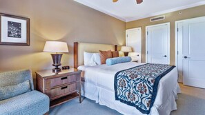 A hotel room with a bed, bedside tables, a lamp, a chair, and a door. - Luxury 1BR in Prestigious Honua Kai K430 (Lahaina)