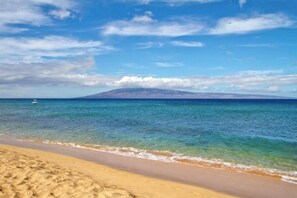 Uma praia com águas azul-claras, areal arenoso e uma montanha ao longe.
