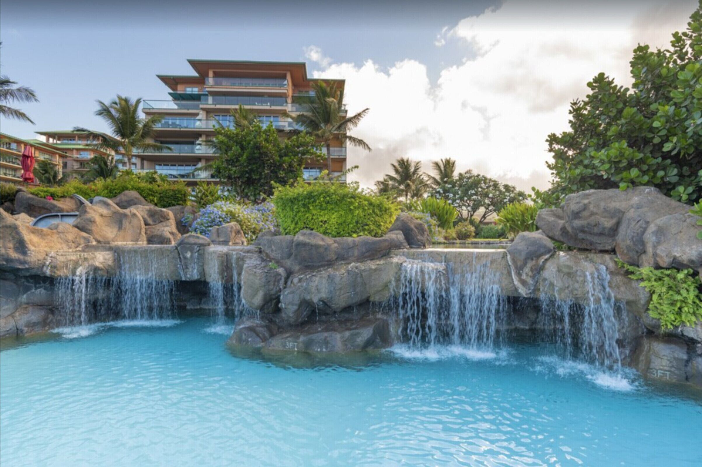 Un complexe hôtelier doté d’une piscine, d’une cascade et d’un bâtiment à plusieurs étages avec des balcons.