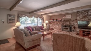 Ein gemütliches Wohnzimmer mit Kamin, Holzbalken, einer Couch und einem Fernseher.