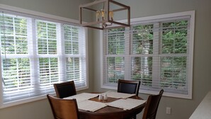 A dining area with a round table, four chairs, and large windows with blinds. - The Great Adventure (McGaheysville)