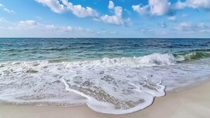Una playa con olas, cielo despejado y un barco a lo lejos.