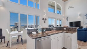 Una cocina amplia con una isla grande, armarios blancos y vista al océano.