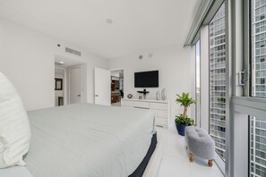 A modern bedroom with a large bed, a TV mounted on the wall, a small kitchenette, and a balcony with potted plants. - ICON W BRICKELL OCEAN VIEW 2BR/2BA #3310 (Miami)