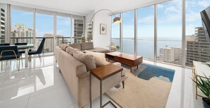 A spacious living room with a large window offering a city view, a sofa, a coffee table, and a dining area with chairs. - ICON W BRICKELL OCEAN VIEW 2BR/2BA #3310 (Miami)