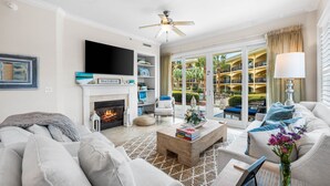A living room with a fireplace, a television, and a view of a pool and building in the background. - Beautiful, FABULOUS Ground Floor Corner Unit @ Adagio E105 (Santa Rosa Beach)