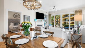 A spacious living room with a large wooden dining table, comfortable seating, and a view of the outdoor balcony. - Beautiful, FABULOUS Ground Floor Corner Unit @ Adagio E105 (Santa Rosa Beach)