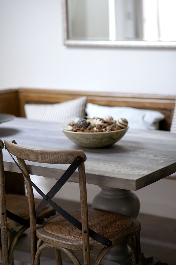 A dining table with a bowl of cereal, a wooden chair, and a bench with pillows.
