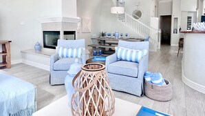 A spacious living room with a fireplace, two sofas with striped cushions, a coffee table, and a staircase leading to another level. - #1 Location, Spacious Beach House, Steps to Fun (Oceanside)