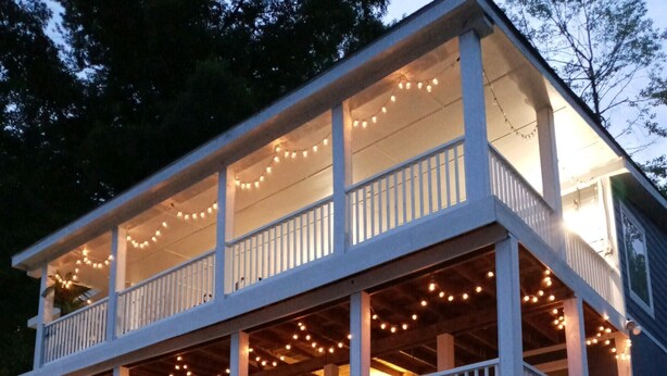 A two-story waterfront house with a wooden deck and string lights. - What a view of our beautiful Lake Jordan. This cabin is sure to charm you .  (Titus)