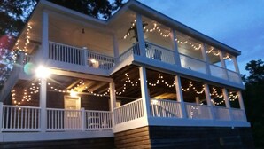 A two-story house with a porch decorated with string lights. - What a view of our beautiful Lake Jordan. This cabin is sure to charm you .  (Titus)