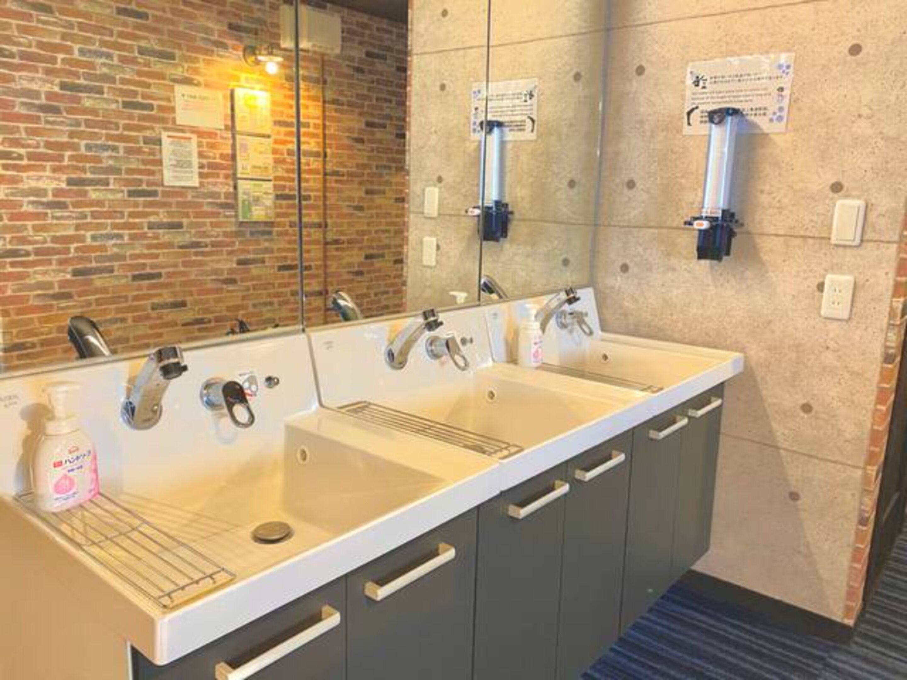 A hotel bathroom with a double sink, a mirror, and a brick wall.