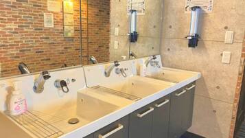 A hotel bathroom with a double sink, a mirror, and a brick wall.