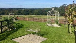 A well-maintained garden with a metal bench, a decorative gazebo, and a wooden fence. - The Farmhouse - Sleeps 12 with Private Grounds (Hailsham)