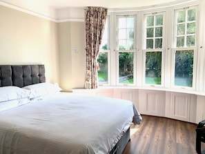 Un dormitorio con una cama grande, una ventana con cortinas y vistas a la vegetación.