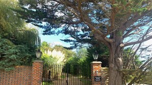 A gated entrance with a brick wall and metal gate, surrounded by trees and a clear sky. - The Farmhouse - Sleeps 12 with Private Grounds (Hailsham)