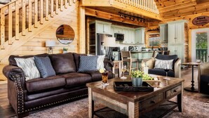 A cozy cabin interior with a wooden staircase, a living room with a brown leather couch, a dining area, and a kitchen with light green cabinets. - Read Our Reviews! Indoor Pool + Outdoor Pool + View (Sevierville)