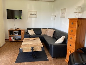 A living room with a black leather sofa, a wooden coffee table, a TV, a wooden cabinet, and a lamp.