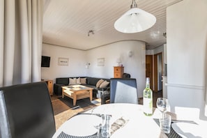 A living room with a sofa, coffee table, and dining table with chairs. There is a bottle and glass on the table.