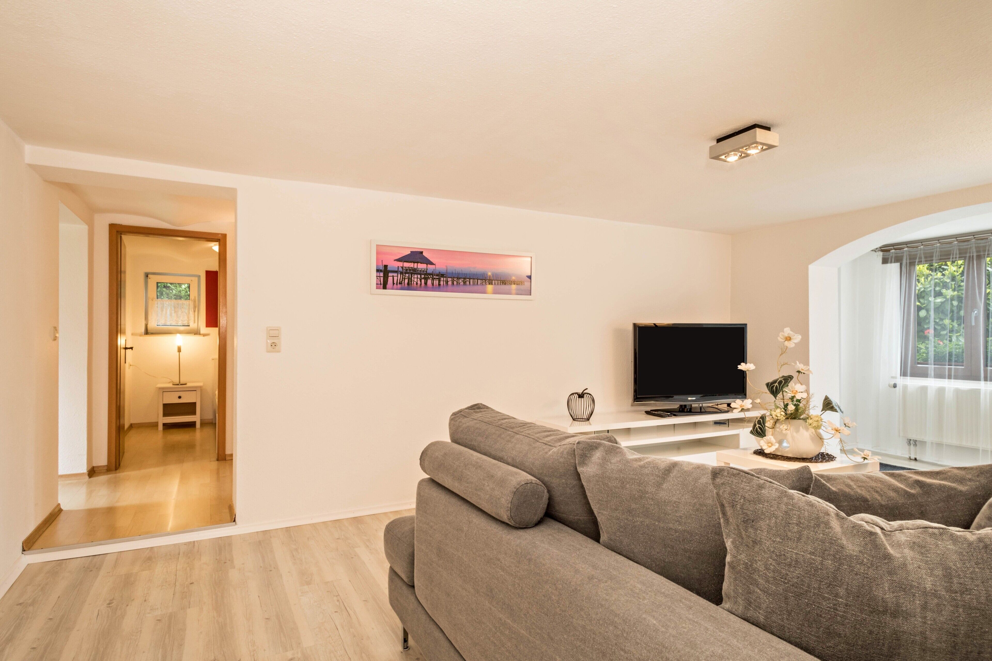 Una sala de estar con un sofá, un televisor de pantalla plana, un cuadro y una ventana con cortinas.