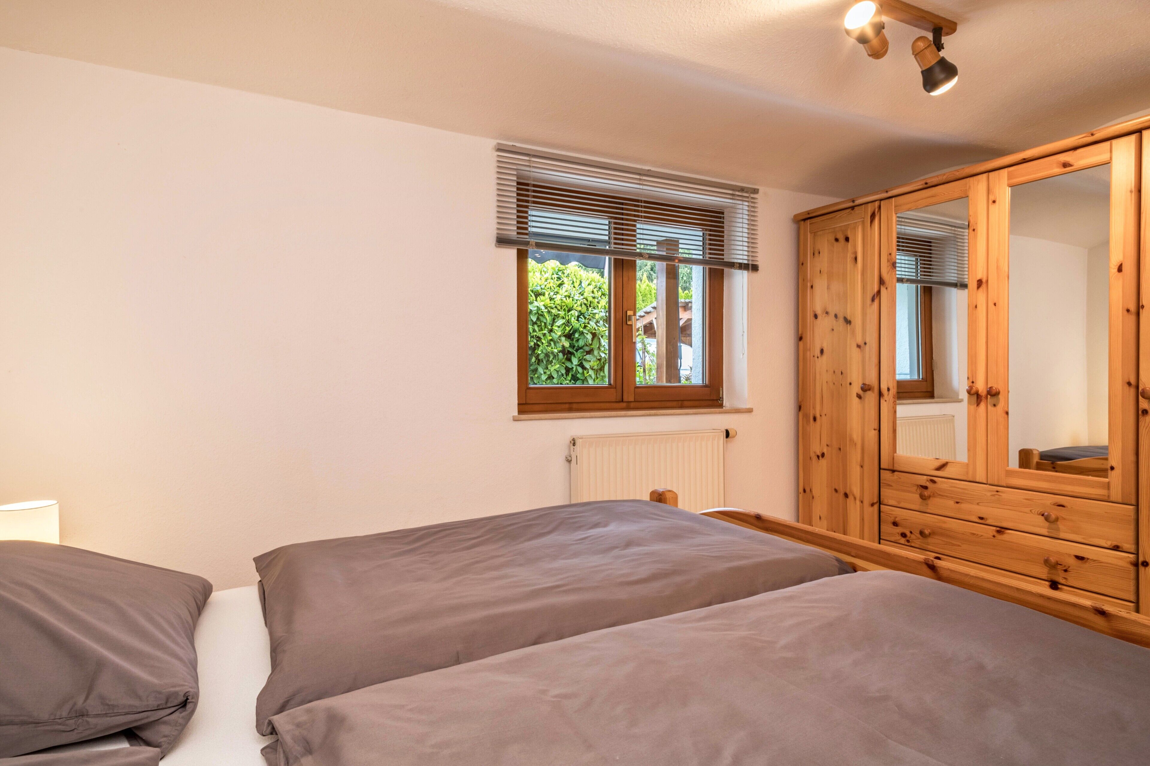 A bedroom with two beds, a wooden wardrobe, a window with blinds, and a radiator.