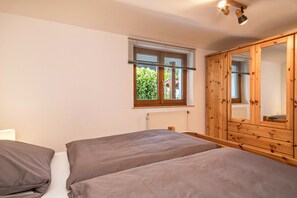 A bedroom with two beds, a wooden wardrobe, a window with blinds, and a radiator.