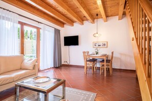 Una sala de estar con sofá, una mesa de comedor con sillas, un televisor montado en la pared y una escalera.