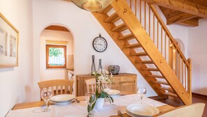 Un coin repas agrémenté d’un escalier en bois, d’une horloge au mur et d’une fenêtre donnant sur un paysage verdoyant.