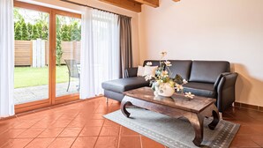 Un salon avec un canapé, une table basse en bois ornée de fleurs et une porte-fenêtre coulissante donnant sur une terrasse.