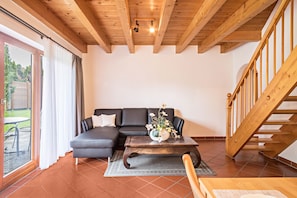 En stue med træloft, en sort sofa, et træsofabord med en vase og en trappe.