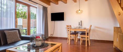 Uma sala de estar com sofá, mesa de centro, mesa de jantar com cadeiras, televisão fixada na parede e escada.