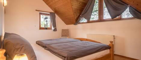 Un dormitorio con una cama de madera, una mesita de noche con una lámpara, una ventana con cortinas y un radiador.