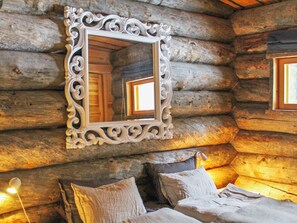 Interior de una cabaña de troncos con una cama, almohadas y un espejo de marco decorativo.