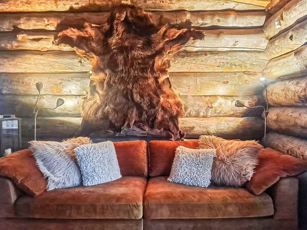 A cozy room with a large fur rug, a brown sofa, and a wooden wall with a fur rug hanging on it.