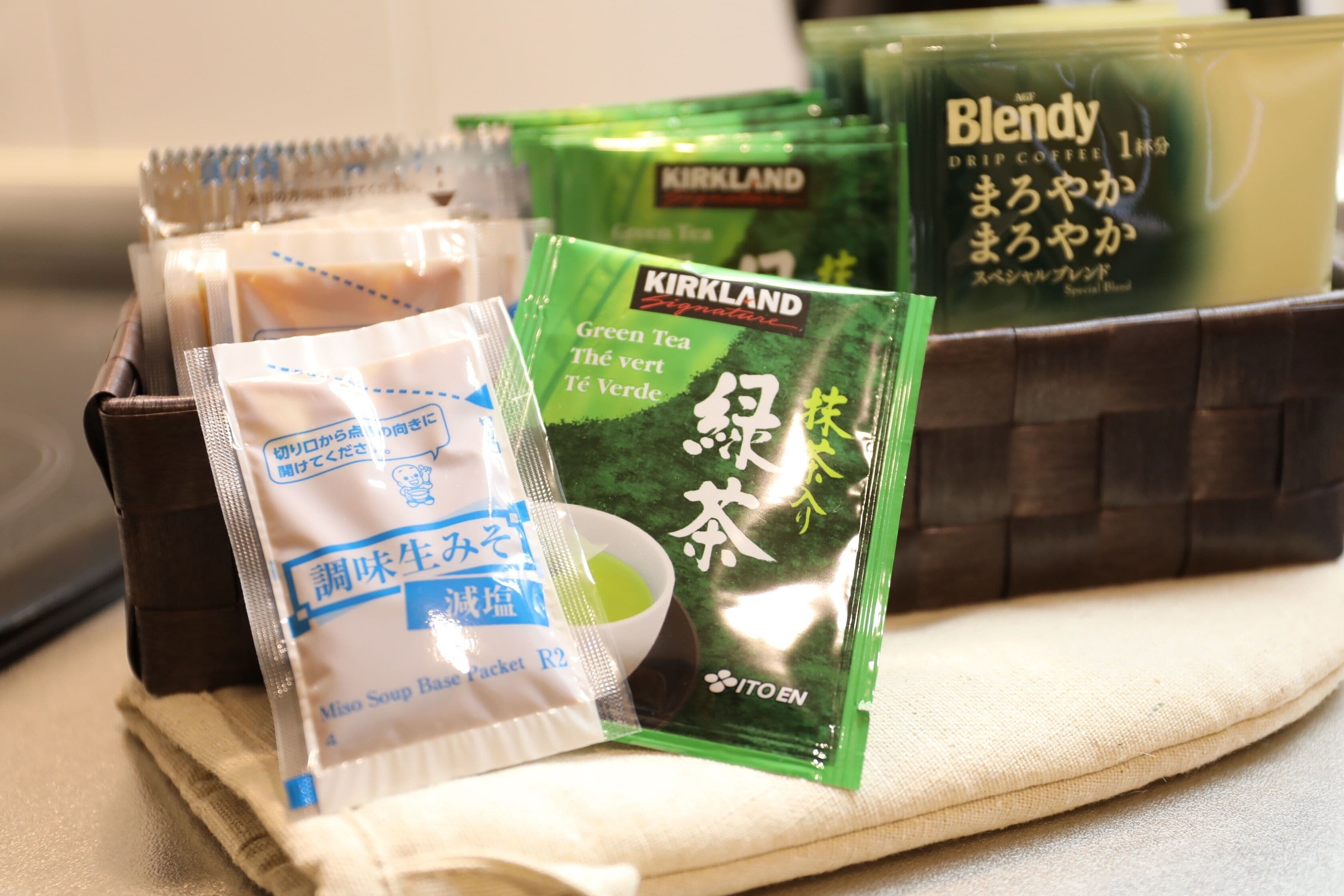 Un plateau contenant divers produits alimentaires emballés, notamment du thé vert Kirkland, un mélange de café Kirkland et un sachet de préparation pour soupe miso.
