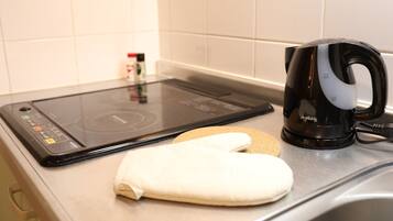 Una cocina con una placa de inducción, un hervidor negro y un guante de cocina blanco sobre la encimera.