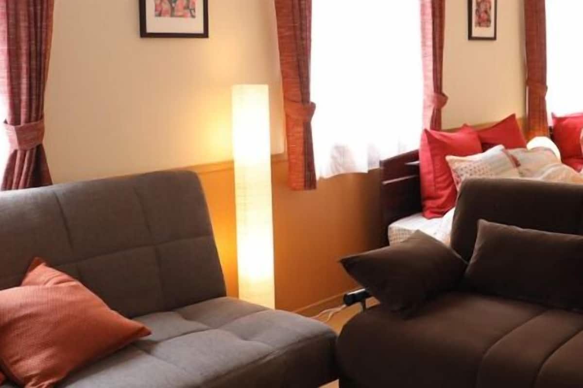 Een hotelkamer met een grijze bank, een bed met rode kussens en een raam met gordijnen.