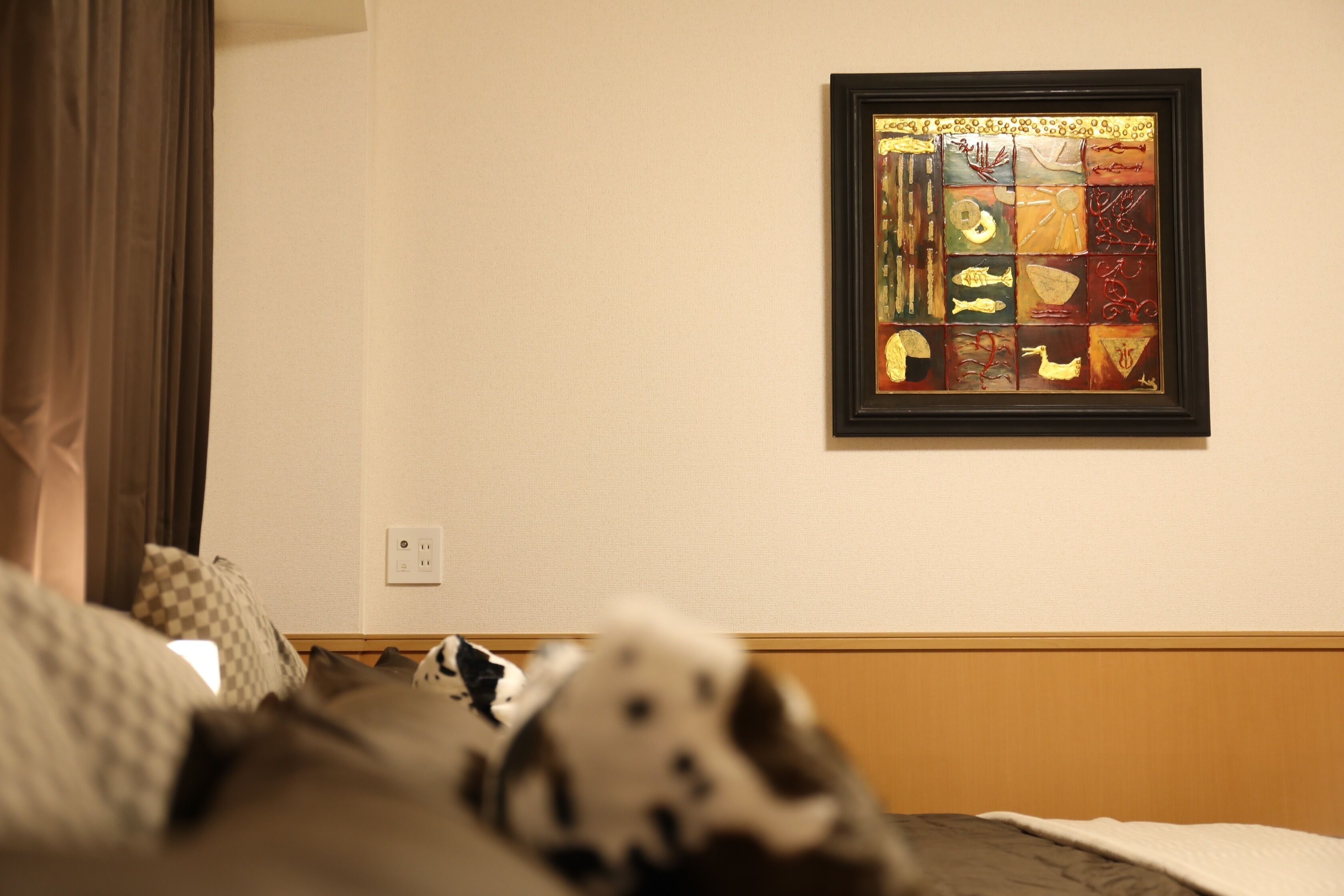 A hotel room with a bed, a framed artwork on the wall, and a power outlet.