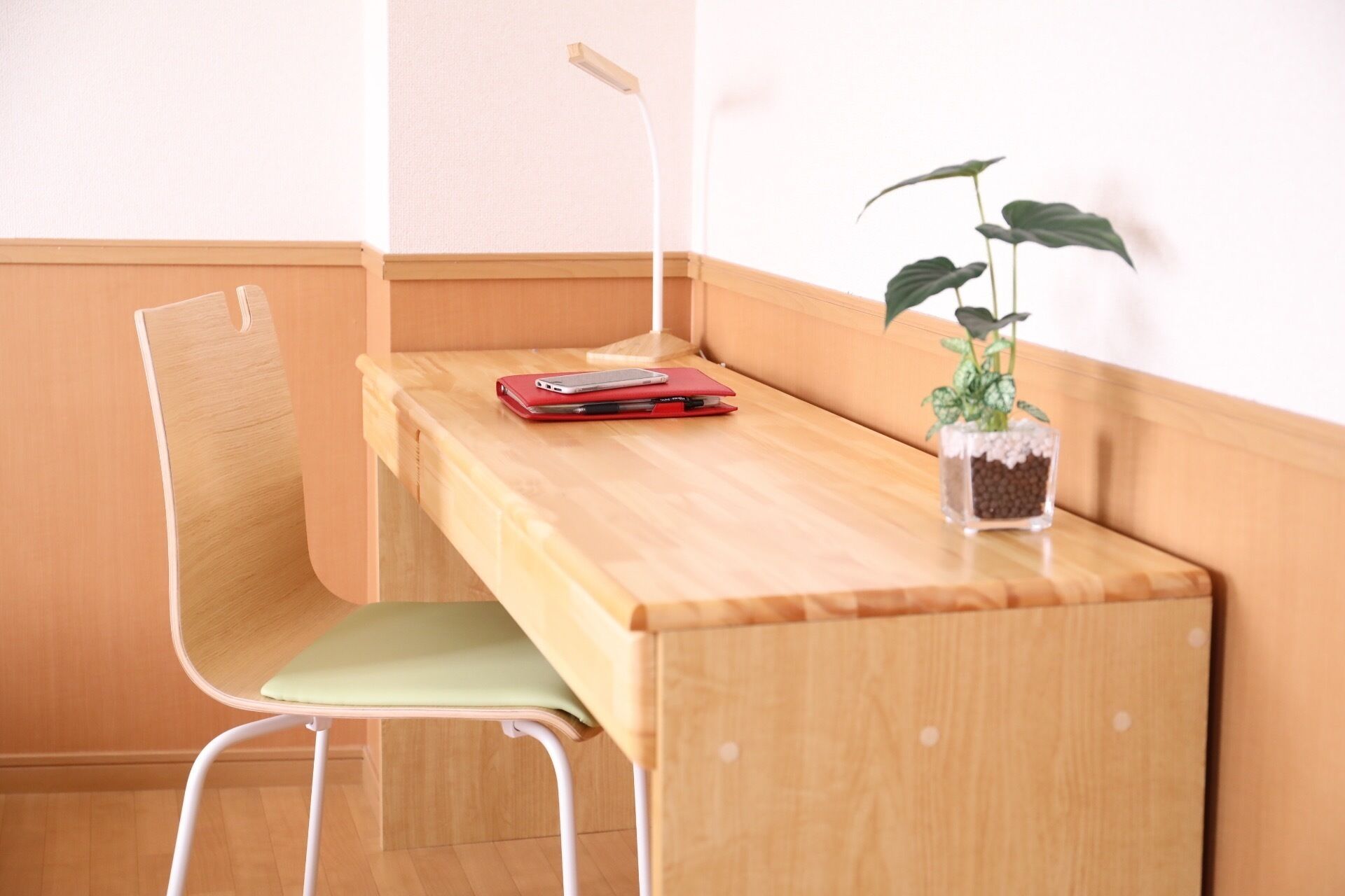 Un bureau d’angle avec une chaise, un carnet rouge et une plante en pot.
