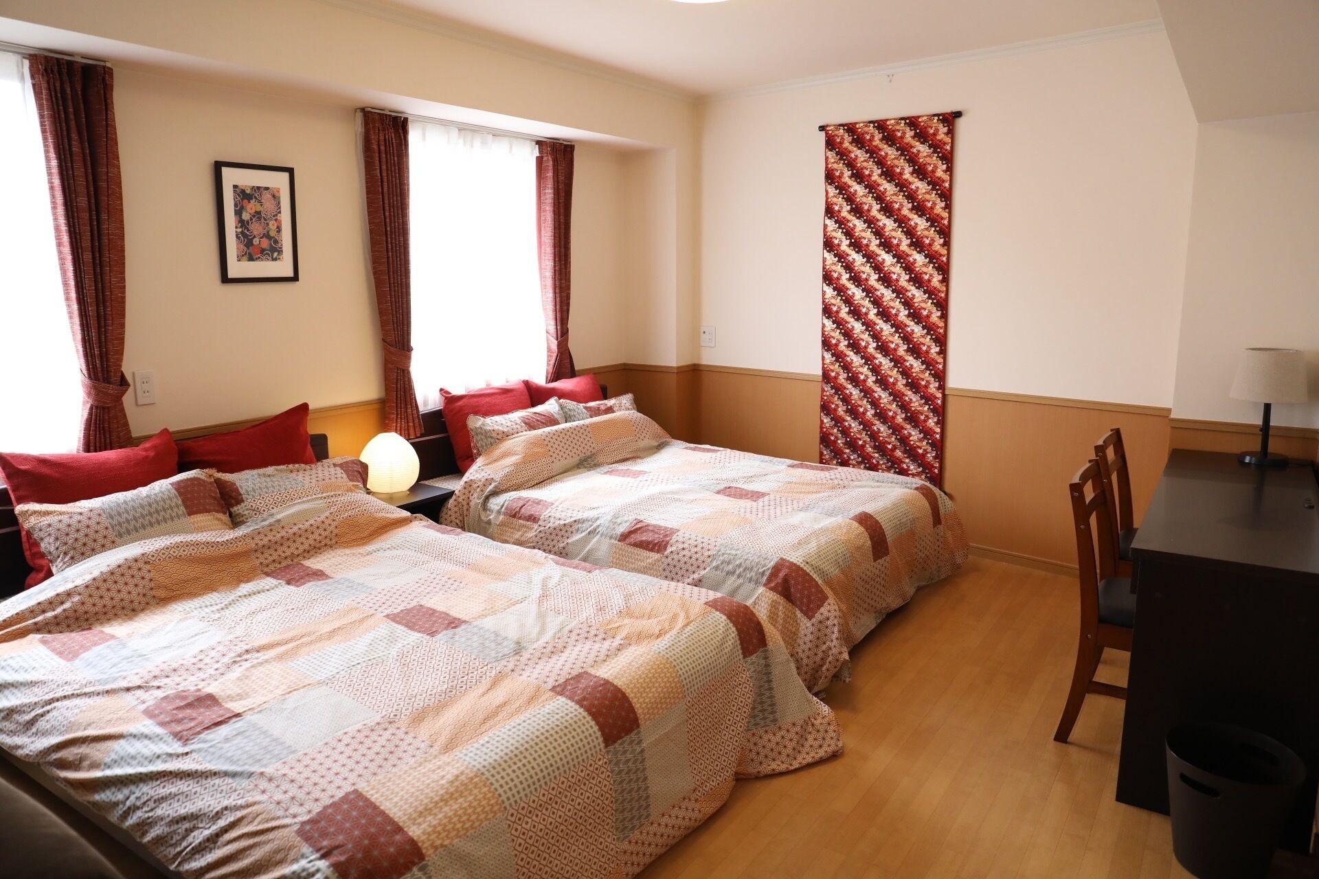 A hotel room with two beds, a desk, a chair, and a window with curtains.