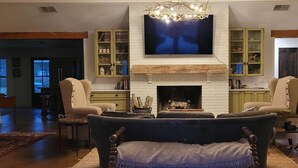Ein Wohnzimmer mit Kamin, einem darüber hängenden Fernseher und zwei Sesseln.