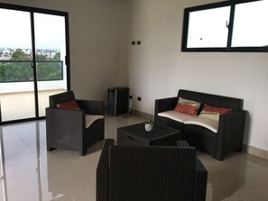 A spacious balcony with a clear view of the cityscape. There are two wicker sofas with cushions and a small table with a plant.