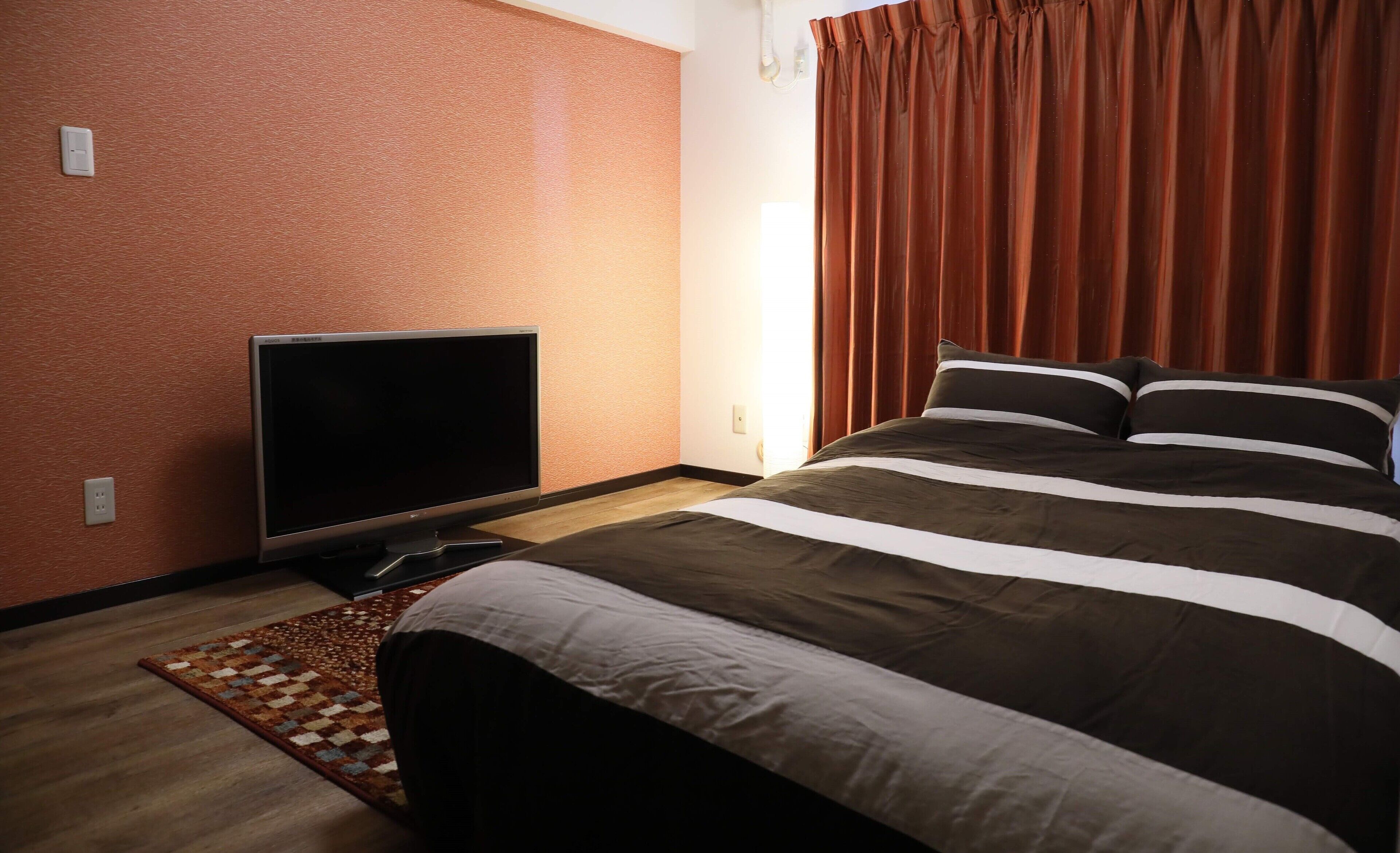 Hotellihuone, jossa on sänky, televisio ja kuviollinen matto.