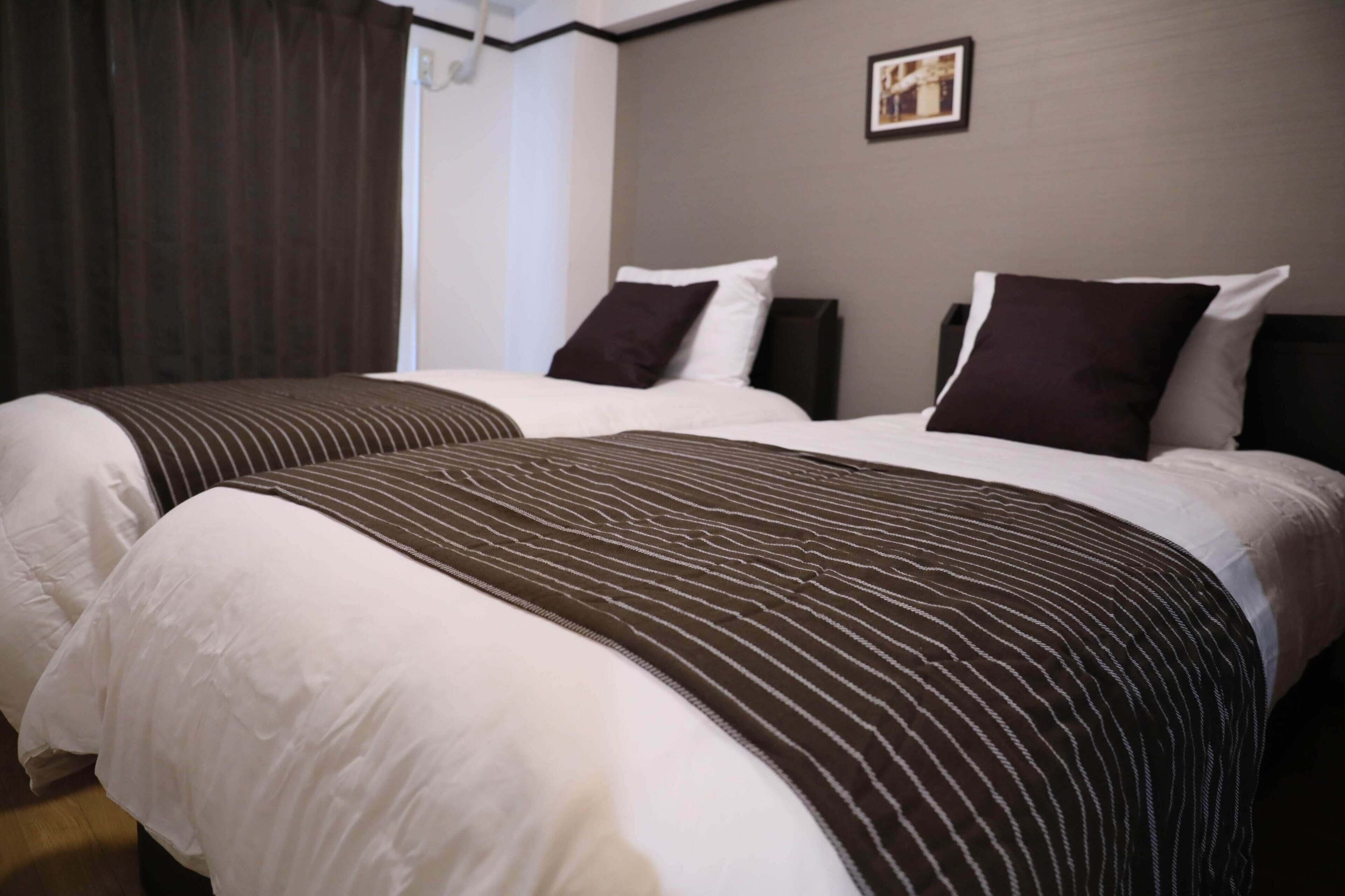 Habitación de hotel con dos camas, cada una con ropa de cama blanca y mantas a rayas marrón oscuro.