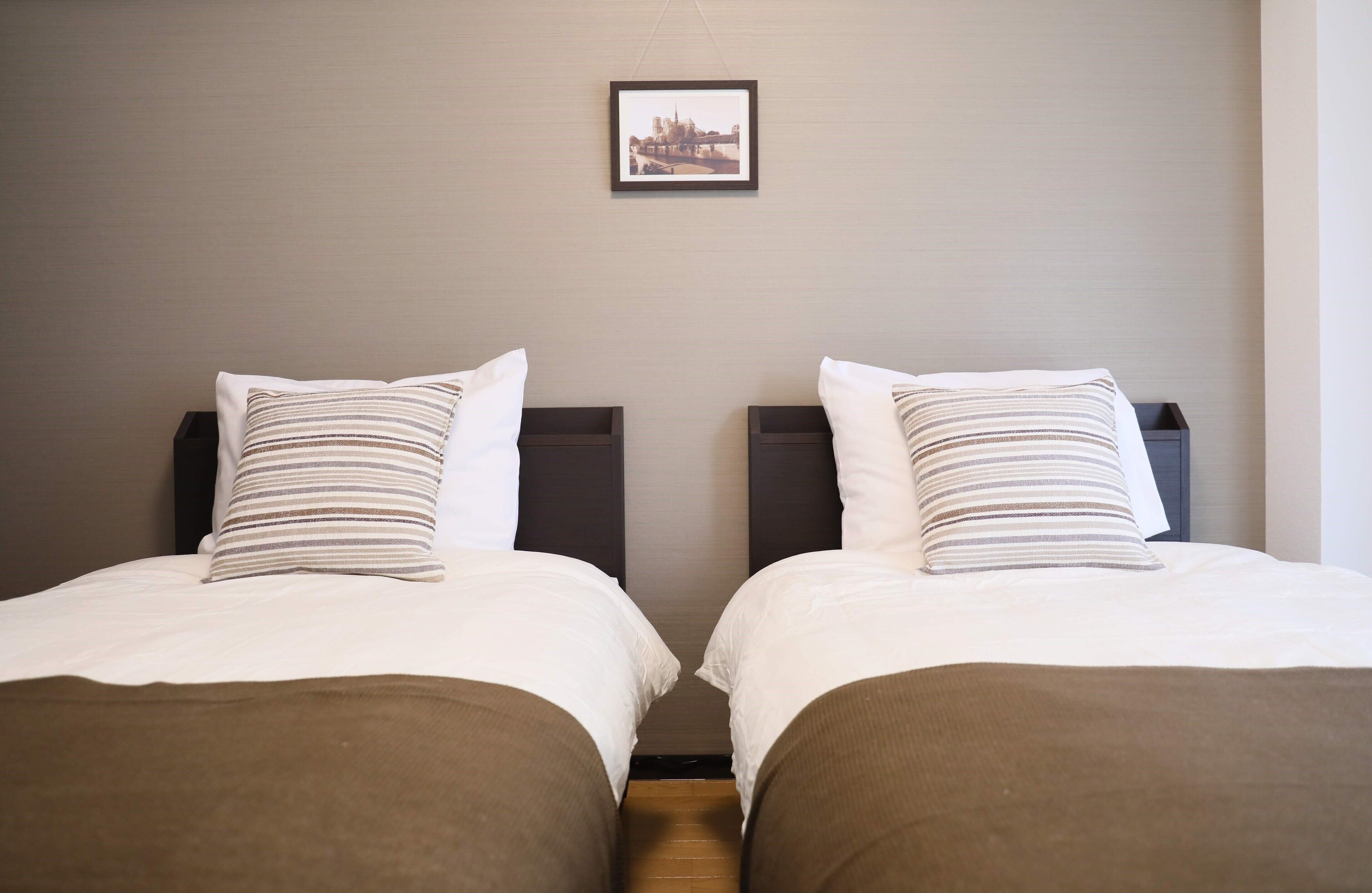 Two twin beds with striped pillows and brown bedspreads, a framed picture on the wall, and a wooden floor.