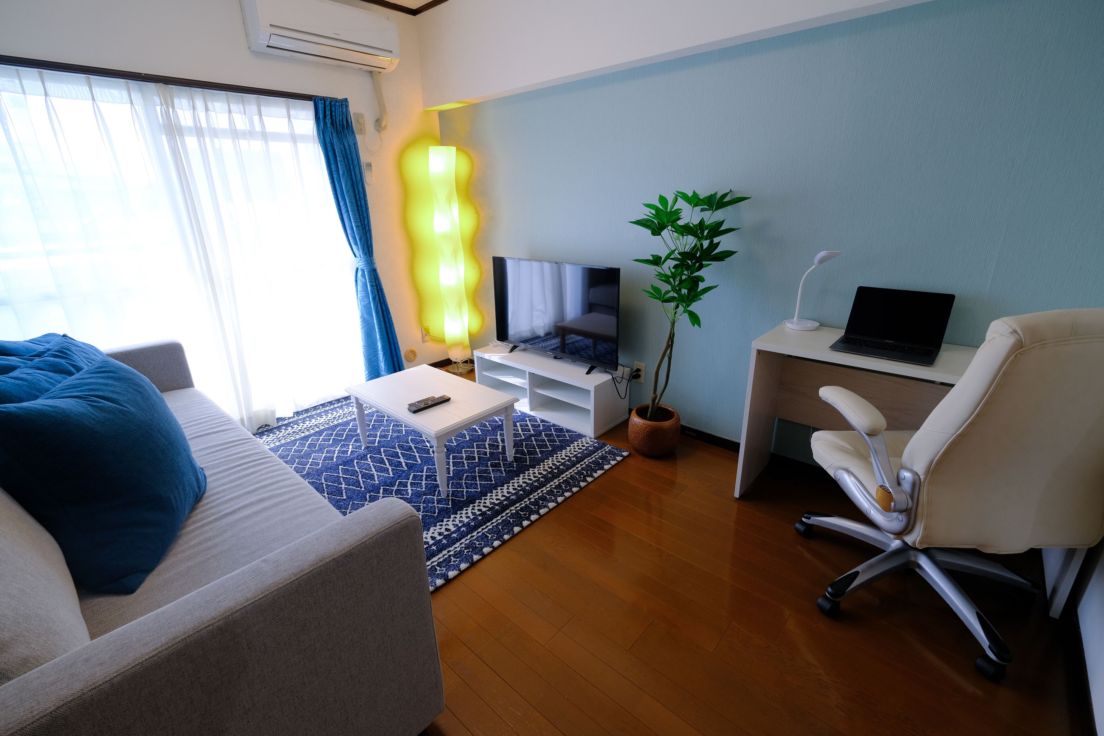 Una sala de estar moderna con un sofá, una mesa de centro, un televisor, un escritorio con una computadora portátil y una planta en maceta.