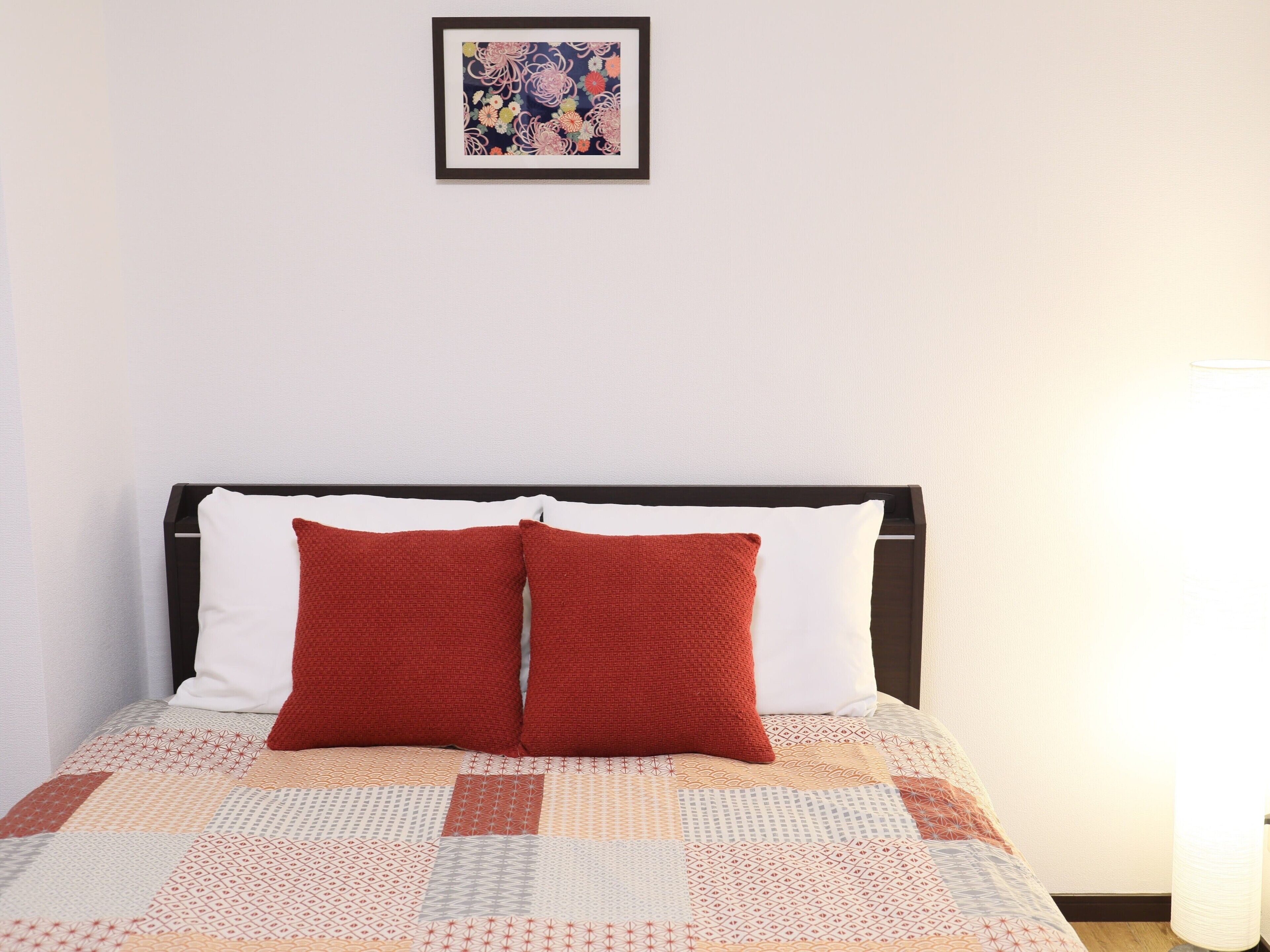 Una cama bien tendida con colcha estampada, dos almohadas y una obra de arte enmarcada encima.