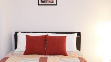 Una cama bien tendida con colcha estampada, dos almohadas y una obra de arte enmarcada encima.
