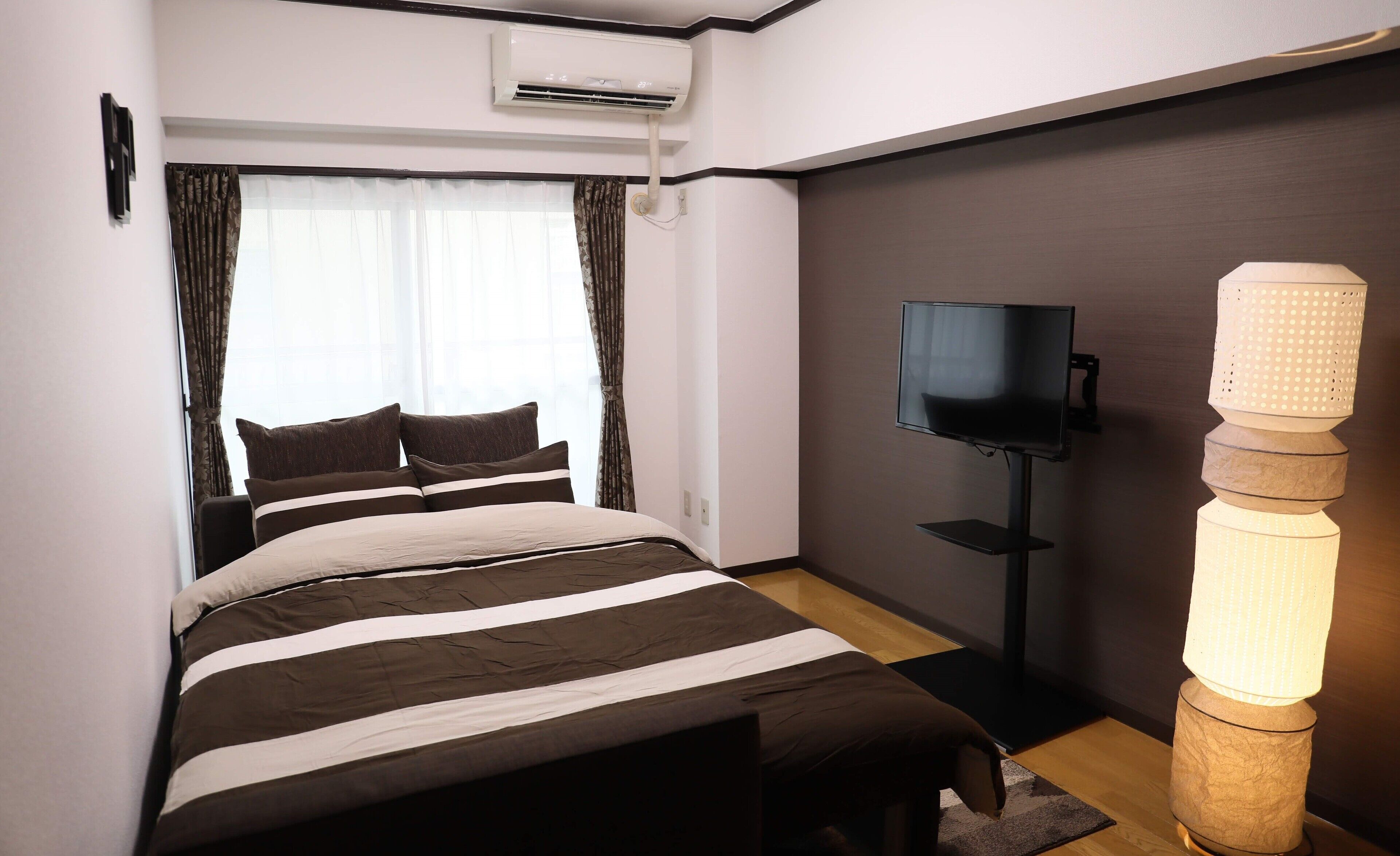 A hotel room with a bed, curtains, a television, and a unique wall-mounted light fixture.